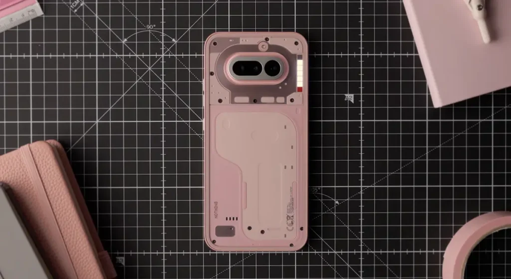Nothing Phone (4a) ピンクモデル。カッティングマット上に置かれ、透明な背面に透過する内部パーツのトーンが調和している。