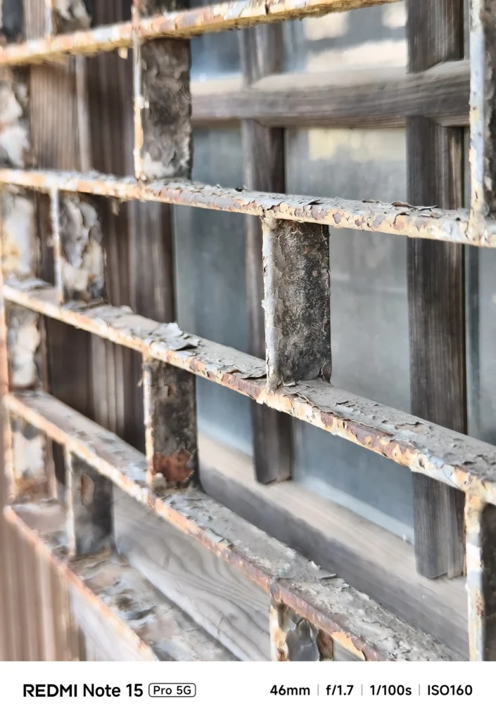 古い窓格子のサビと塗装剥がれを望遠でクローズアップ、木枠の質感も見える（Redmi Note 15 Pro 5G＋1.75x望遠／約81mm相当）