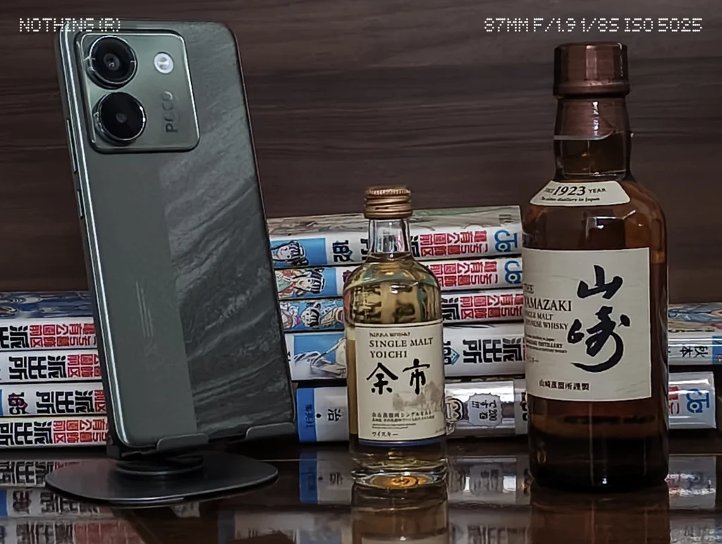 Nothing Phone 3a Liteで暗めの屋内に置いたスマホ、ウイスキーボトル、漫画本をズーム撮影した作例