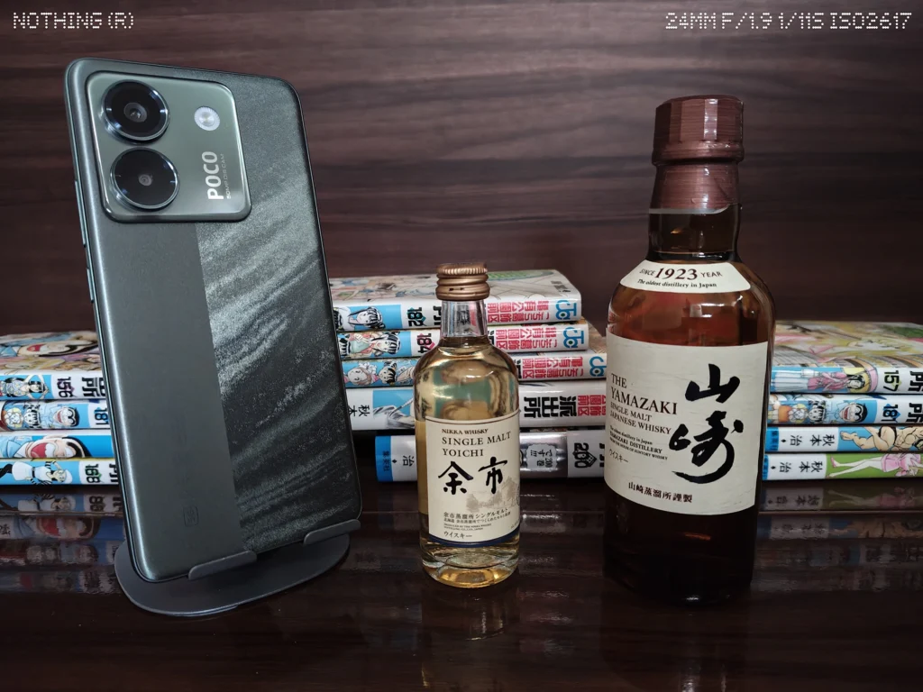 Nothing Phone 4a Proで暗めの屋内に置いたスマホ、ウイスキーボトル、漫画本を等倍撮影したカメラ作例