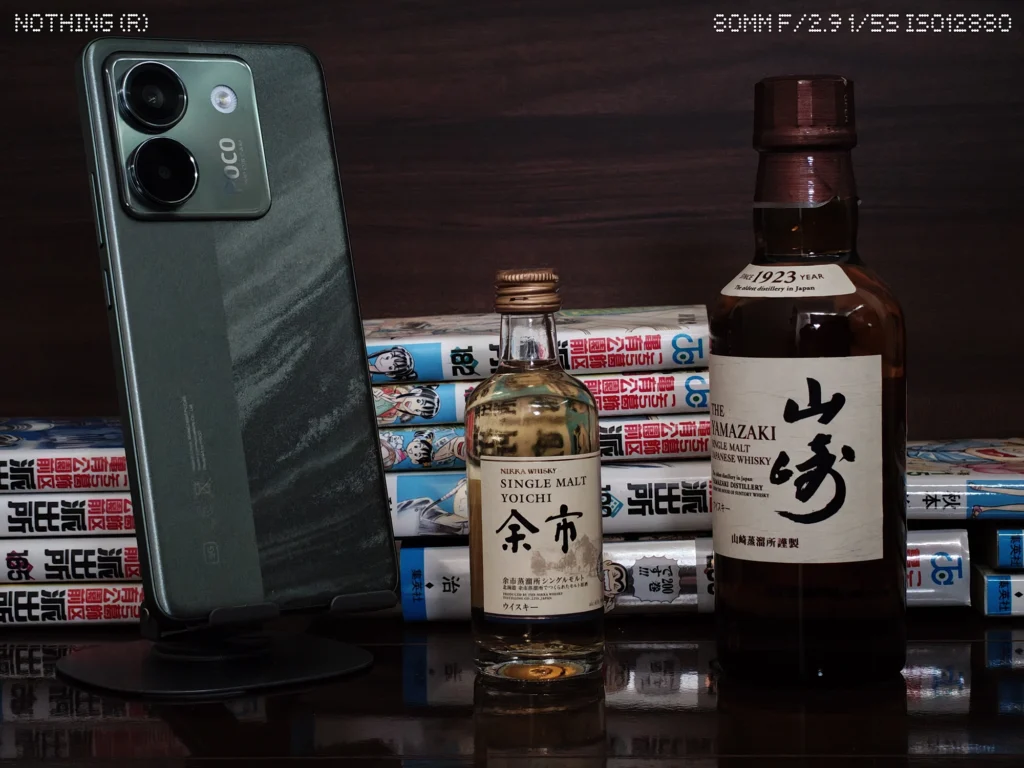 Nothing Phone 4a Proで暗めの屋内に置いたスマホ、ウイスキーボトル、漫画本をズーム撮影したカメラ作例
